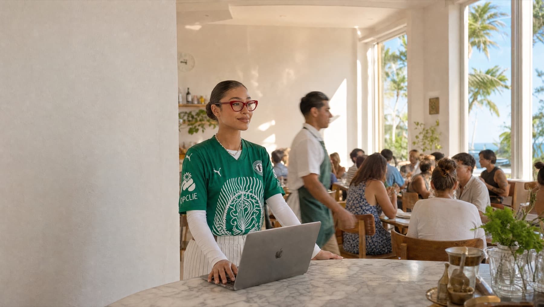 Una moza con su laptop en la barra de un salón lleno, al mediodía